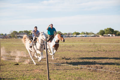 Men riding horse on field against sky