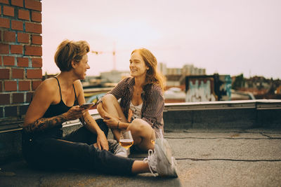 Happy female friends talking while sitting on terrace in city during rooftop party