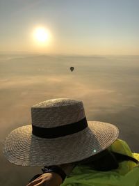 Person holding hat against sky during sunset