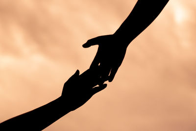 Silhouette people holding hands against sky during sunset