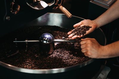 Cropped hand of man holding coffee beans over cooling rack in roaster