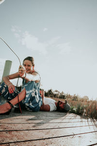 Young woman using mobile phone while sitting against sky