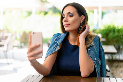 Young woman using mobile phone while sitting at sidewalk cafe