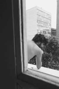 Shirtless man standing in balcony seen through window