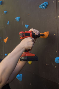 Unrecognizable mechanic using electric screwdriver and fixing grips on climbing wall in gym