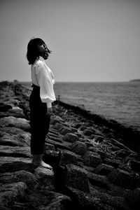 Woman standing on rock at beach against sky