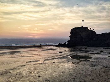 Rocks on beach against sky during sunset