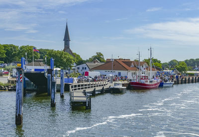 Sailboats in river by buildings against sky