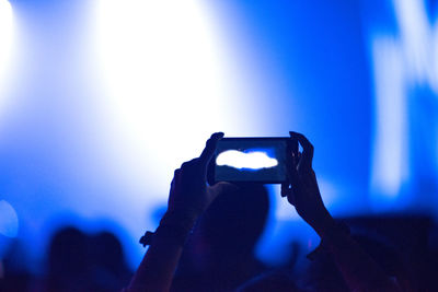 Rear view of hands photographing through smart phone at music concert