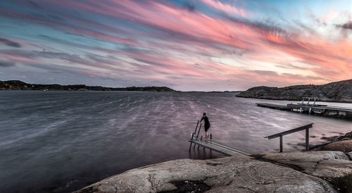 Rear view of woman on pier at lake against cloudy sky during sunset