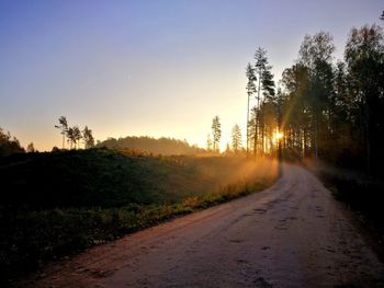 Road amidst trees against sky during sunset