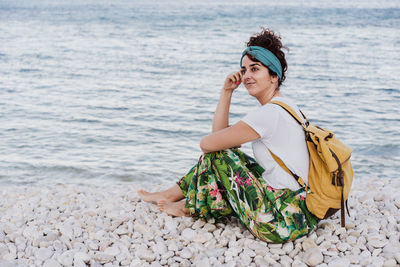 Woman looking away while sitting on sea shore