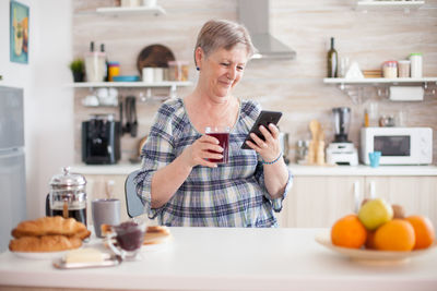 Smiling senior woman using mobile phone at kitchen