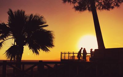 Silhouette people standing on beach against sky during sunset