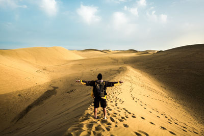 Rear view of man with arms outstretched while standing at desert