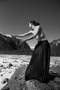 Woman sitting on rock against sky