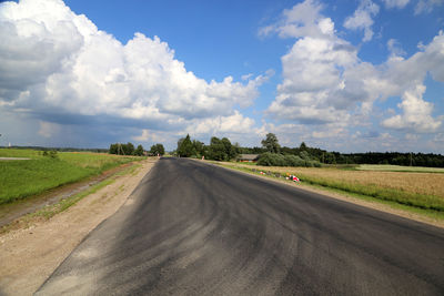 Road passing through field against cloudy sky