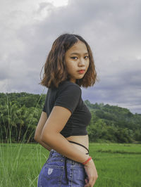 Young woman standing on field against sky