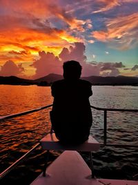 Silhouette man sitting by sea against sky during sunset