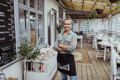 Portrait of confident female owner with arms crossed standing in restaurant