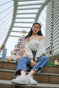 Portrait of young woman sitting against built structure