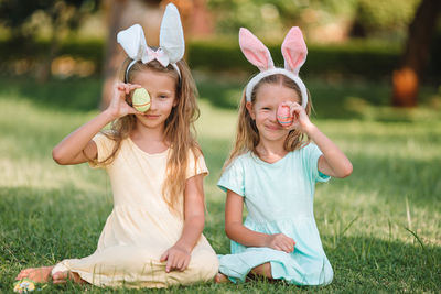 Sisters holding easter eggs while sitting at lawn