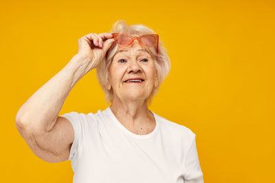 Senior woman holding sunglasses against yellow background