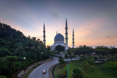 Road amidst buildings against sky during sunset