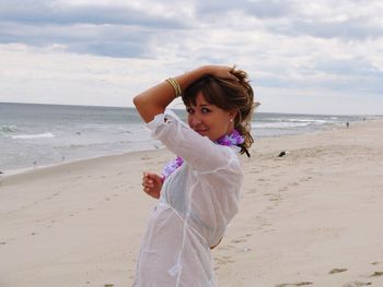 Portrait of beautiful woman posing while standing on beach against cloudy sky