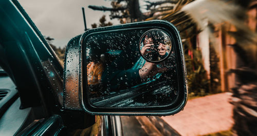 Close-up of young man photographing with camera reflecting on wet side-view mirror