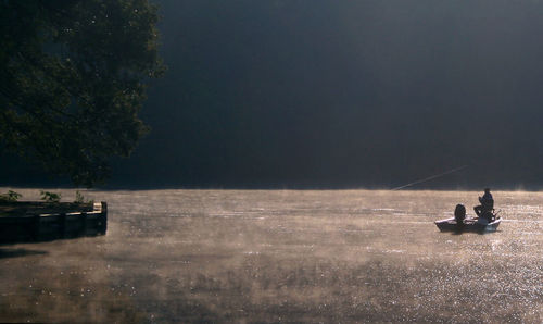 Man sitting on boat in lake against sky