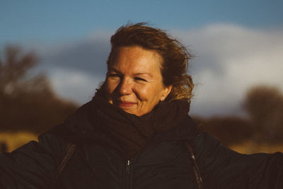 Mature woman wearing warm clothing looking away while standing against cloudy sky