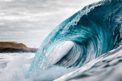 Waves splashing in sea against cloudy sky