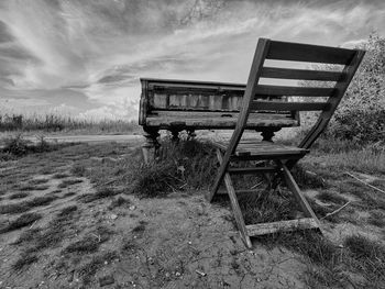 Abandoned bench on field against sky