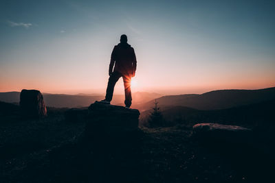 Rear view of silhouette man standing on rock against sky during sunset