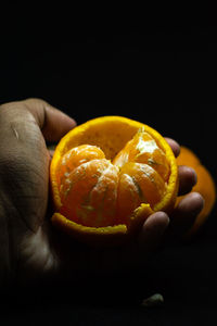 Close-up of hand holding orange fruit against black background