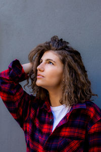 Portrait of young happy sensual woman with curly hair in red shirt on grey background, look up