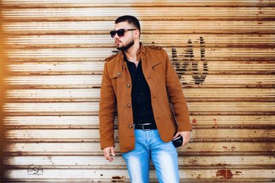 Young man standing against wooden wall