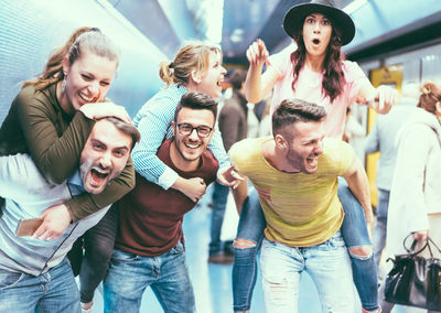 Happy men giving piggyback to girlfriends at railroad station