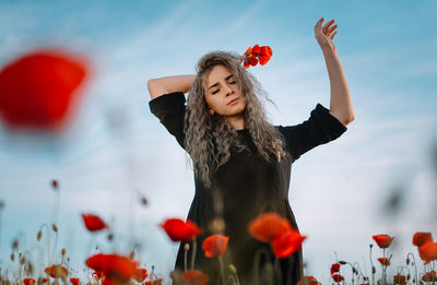 Beautiful young woman in black dress with flowers in poppy field in summer