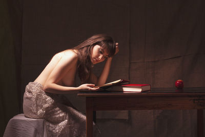 Shirtless woman reading book while sitting on table