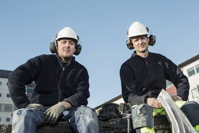 Portrait of confident workers at construction site against clear blue sky