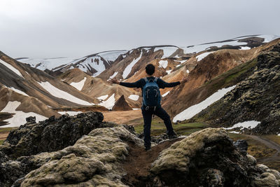 Rear view of woman standing on rock against sky