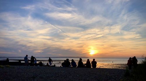 Silhouette people on beach against sky during sunset
