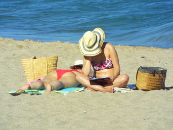 Women sunbathing at beach against sea