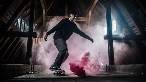 Full length of man skateboarding by red smoke