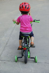 Rear view of boy wearing red helmet riding bicycle on road