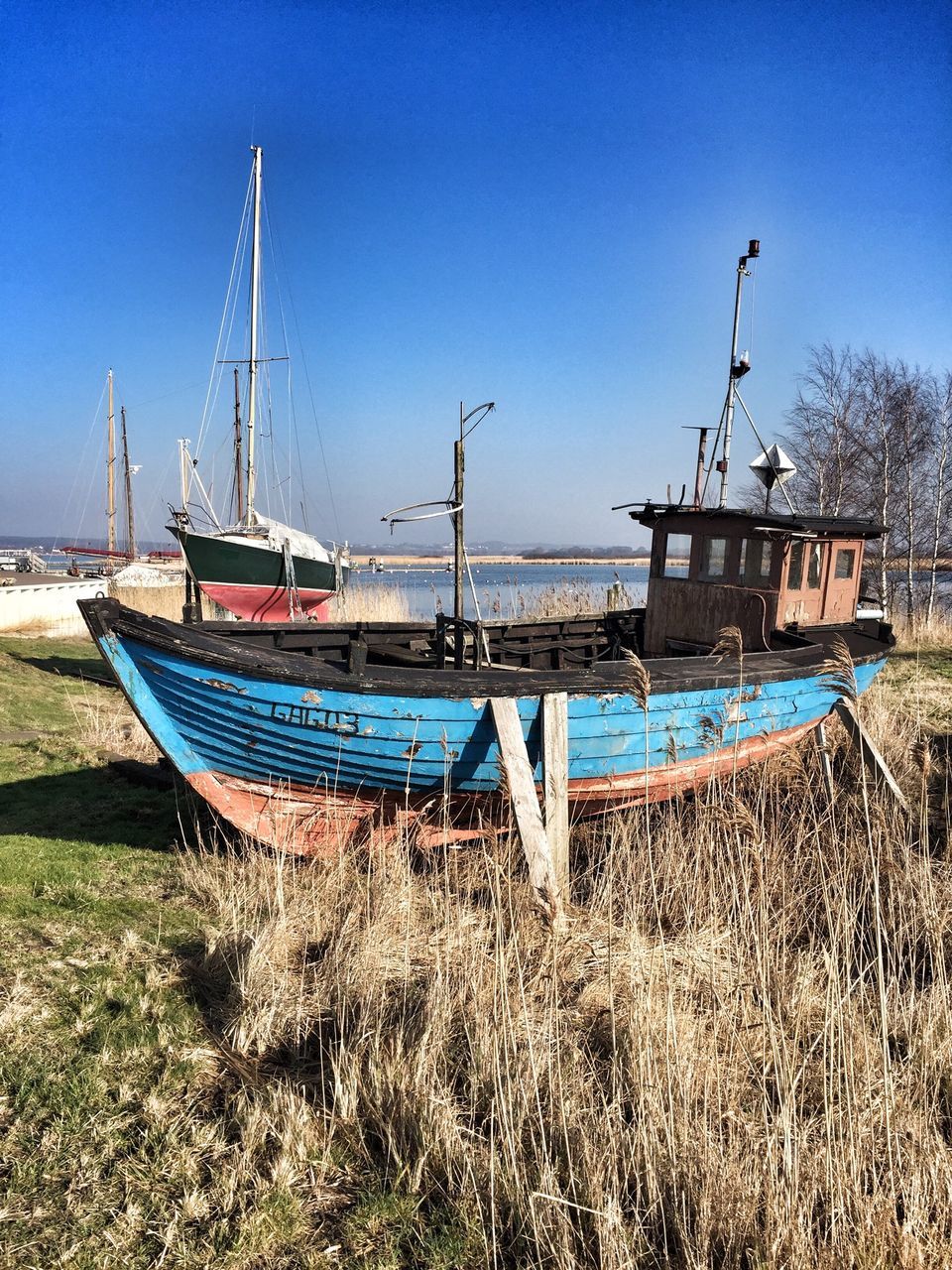 moored, nautical vessel, water, boat, blue, transportation, clear sky, mode of transport, sea, grass, tranquility, beach, tranquil scene, nature, shore, sunlight, copy space, sky, day, harbor