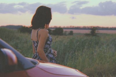 Rear view of woman on field against sky during sunset