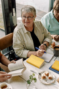 High angle view of smiling senior woman with pen and diary sitting by female friend in cafe